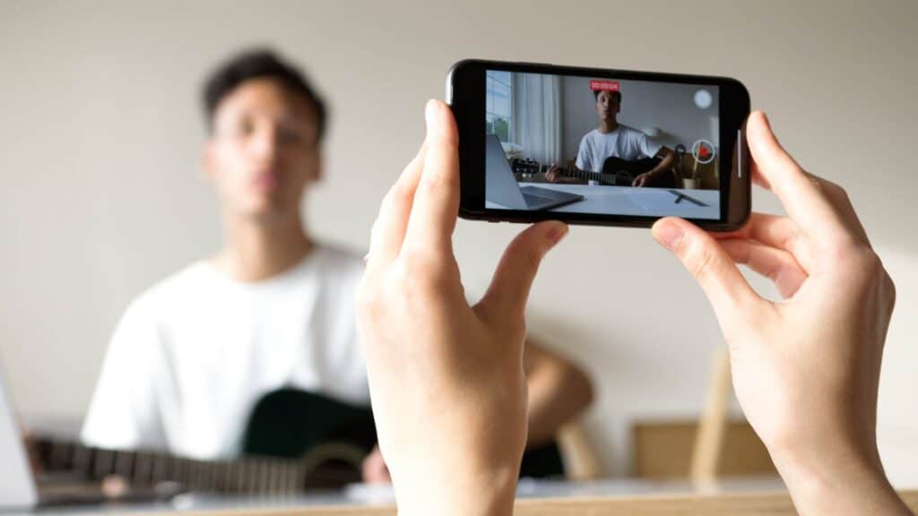 person recording a man playing guitar