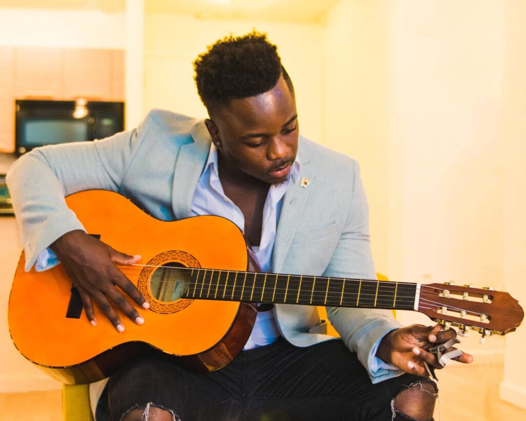 man wearing blue coat and black distressed bottoms holding brown classical guitar