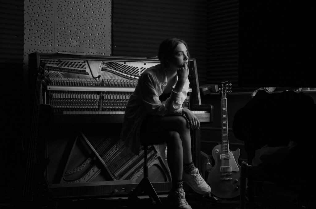 grayscale photo of woman sitting in front of a piano